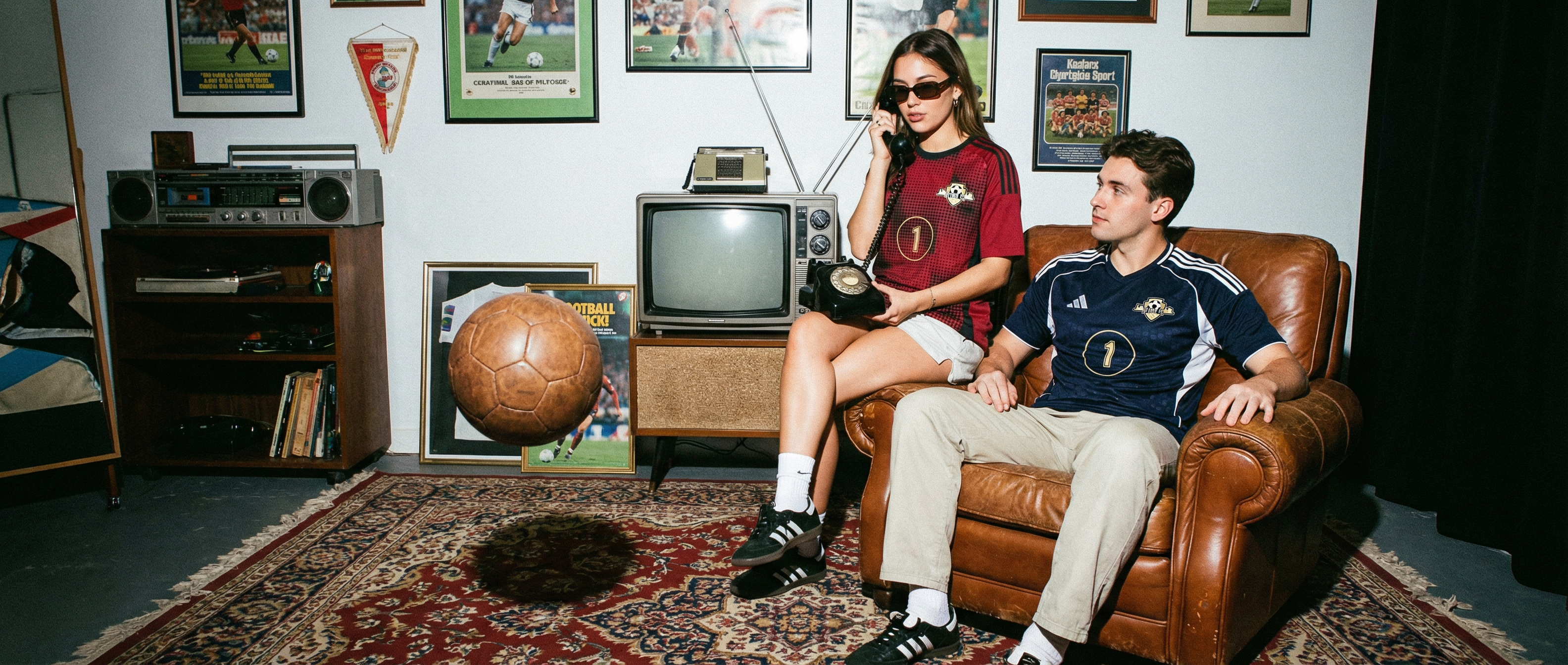 Two people sitting on a leather couch in a room with sports memorabilia.